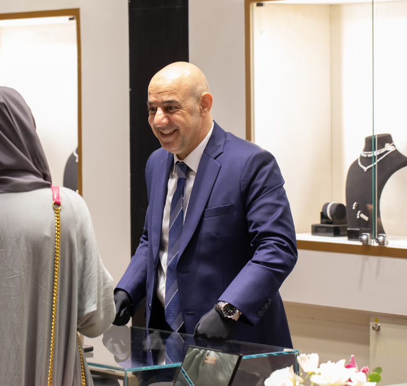 A man dressed in a formal suit, exuding professionalism and elegance, stands in front of a buyer who is trying on a watch